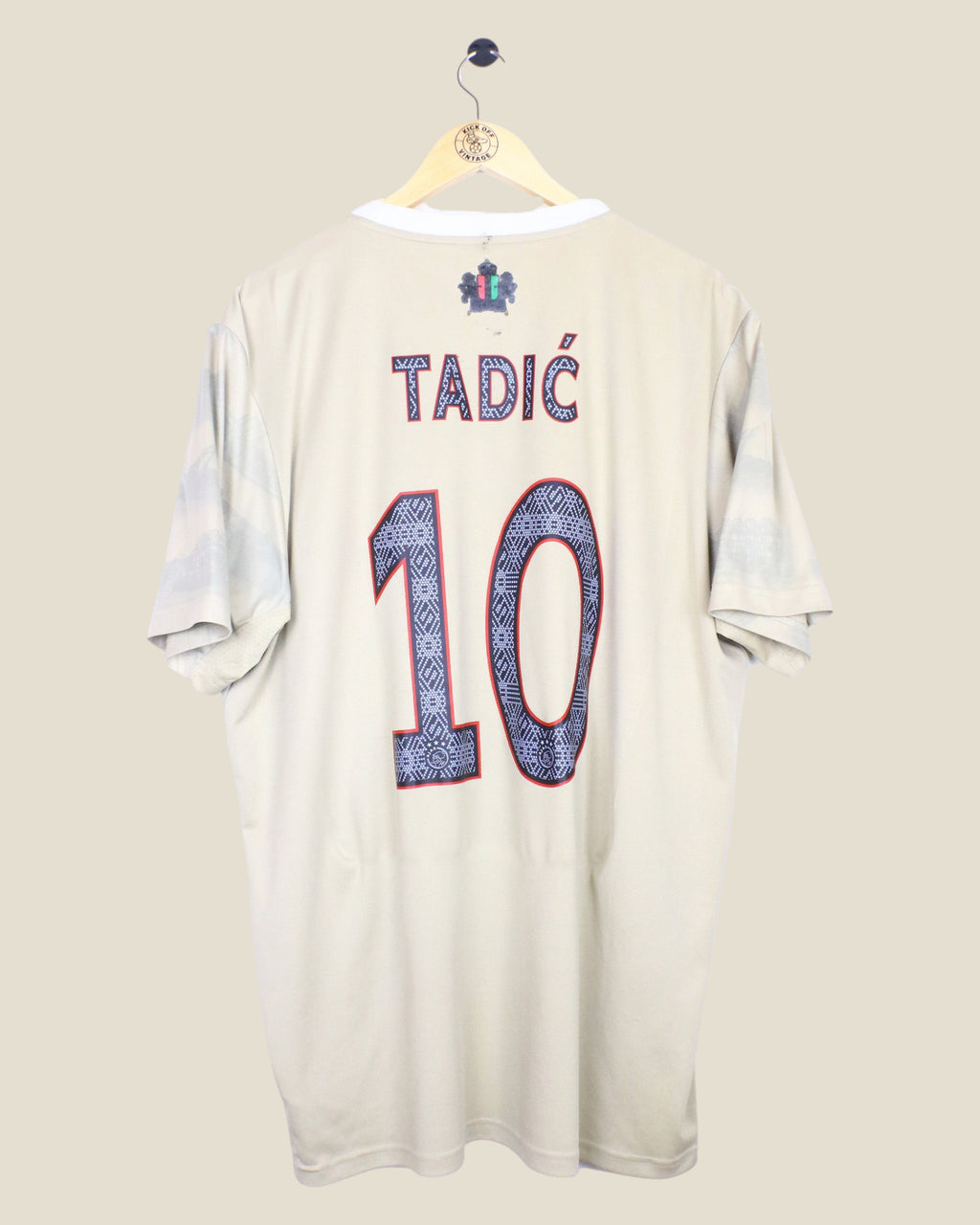 Kick Off Vintage Ajax 2022/23 third football shirt with Tadic 10 nameset on the back, beige jersey on a hanger.