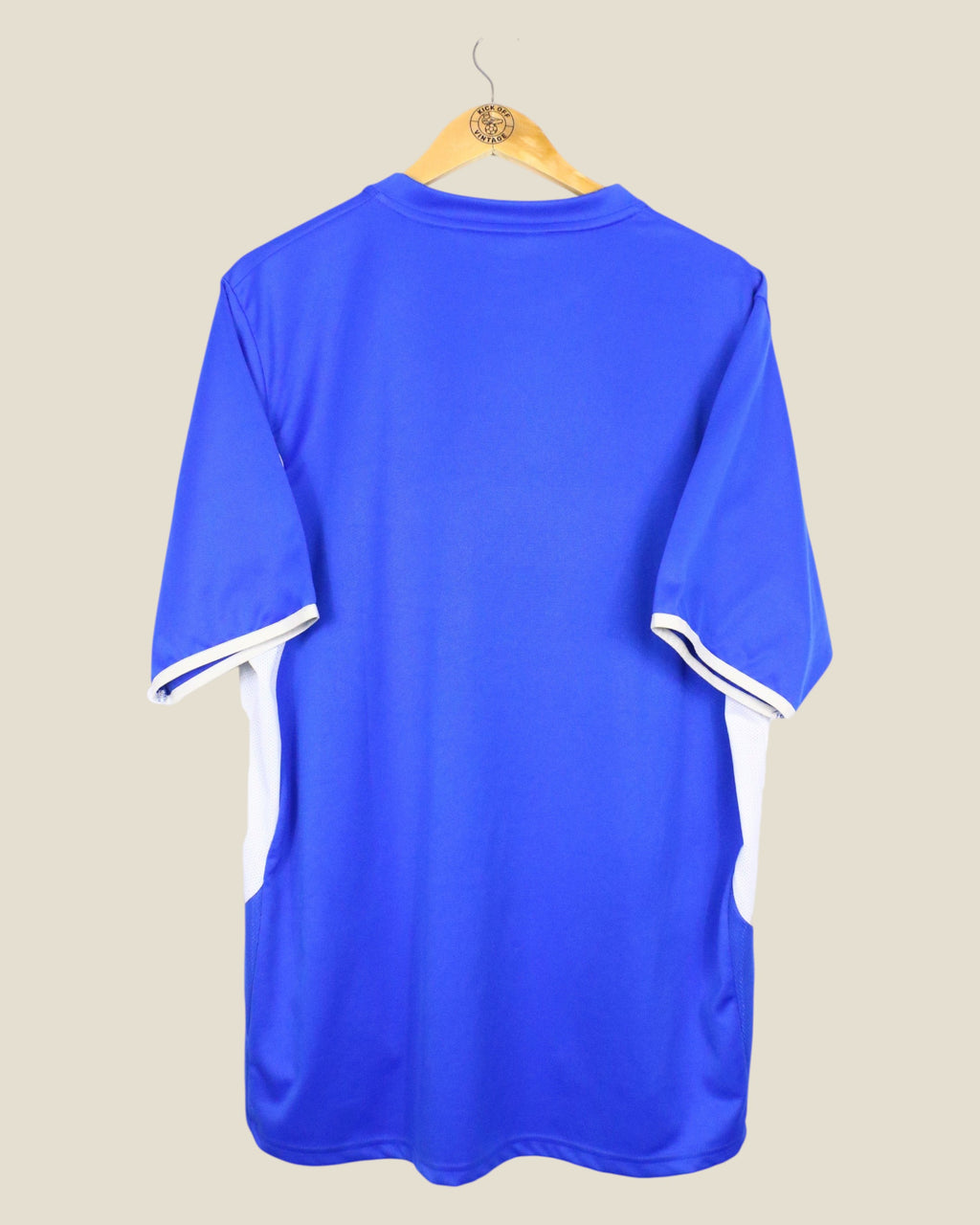 Back view of a blue Kick Off Vintage Millwall 2006/07 home football shirt with white side panels on a wooden hanger.